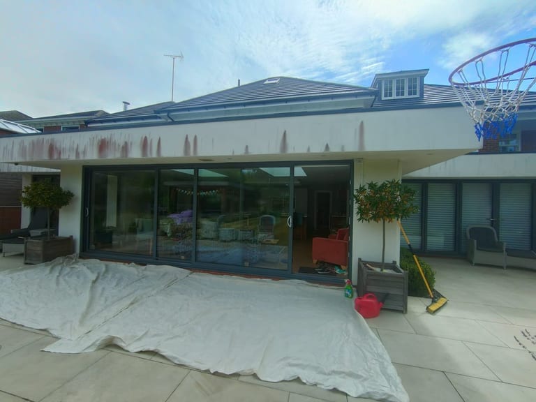 Exterior render painting in progress with surfaces protected